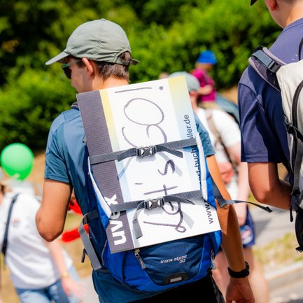 Junger Mann mit Motivationsschild am Rucksack