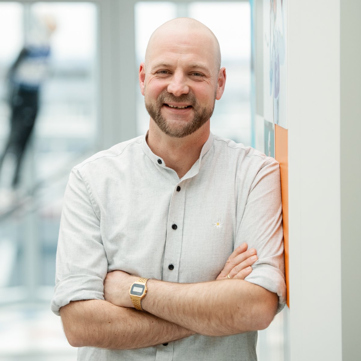 Ein Mann lehnt sich mit verschränkten Armen an einer Wand an und lächelt in die Kamera