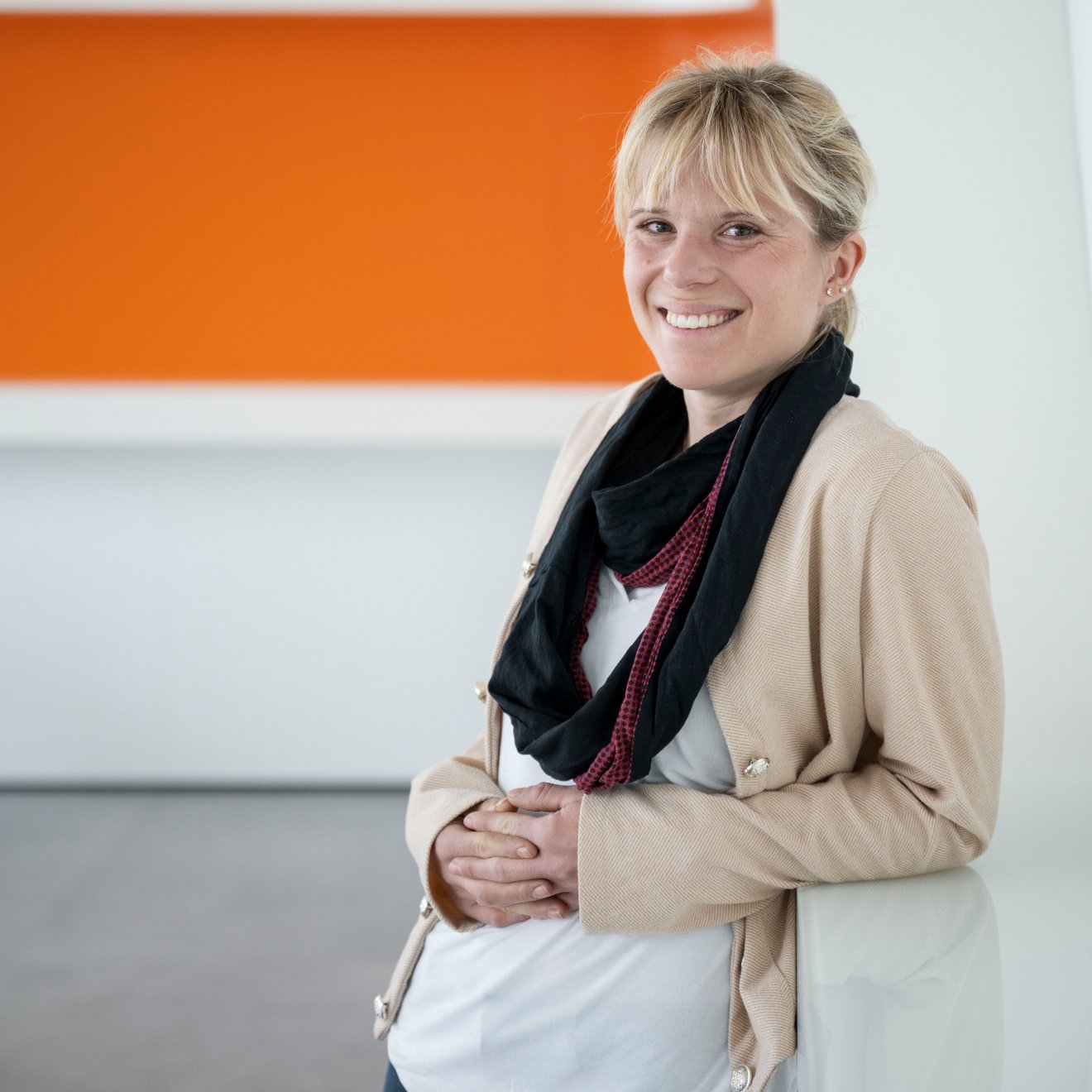 Eine Frau steht vor einem orange-grauen Hintergrund und lächelt