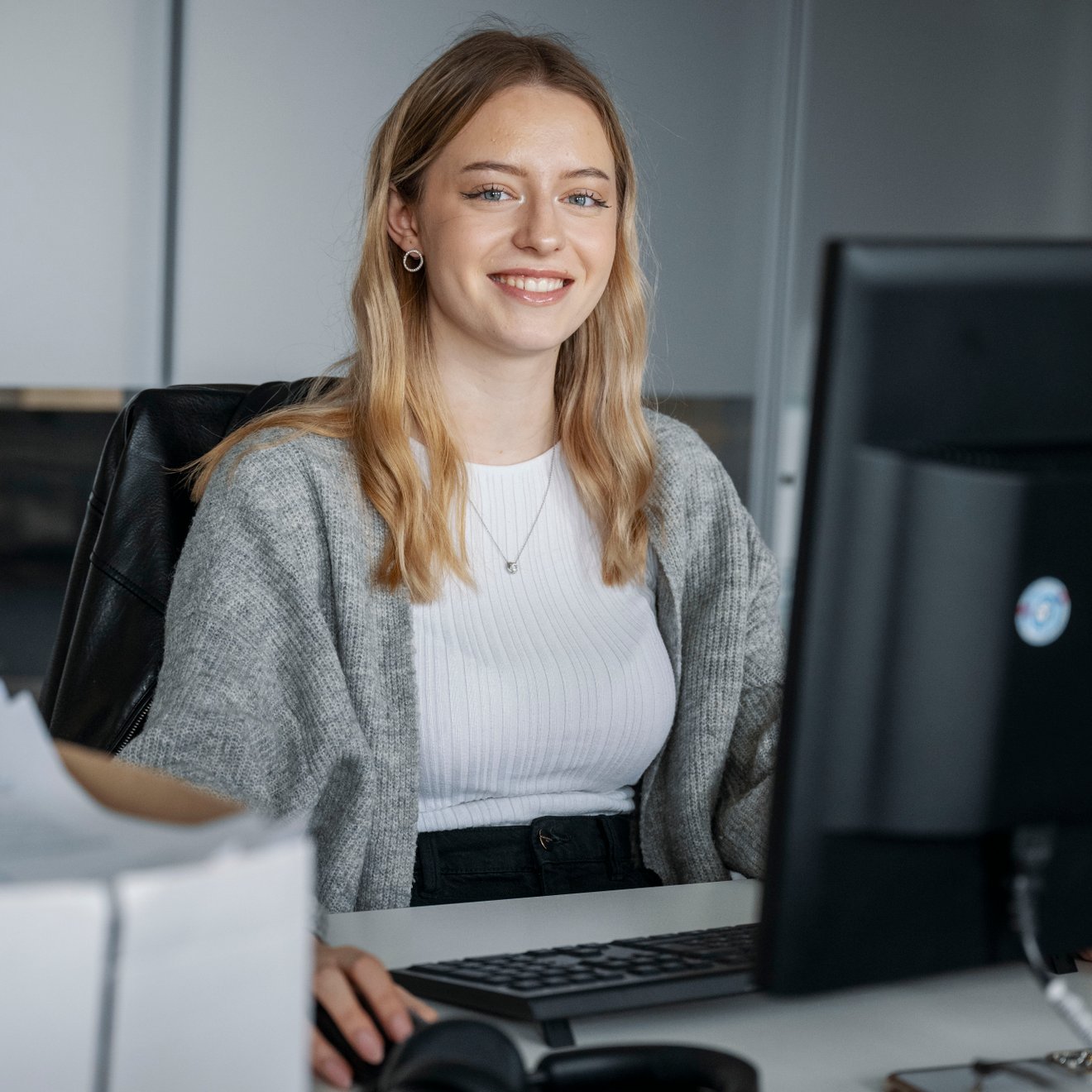 Eine junge Frau sitzt am PC und lächelt