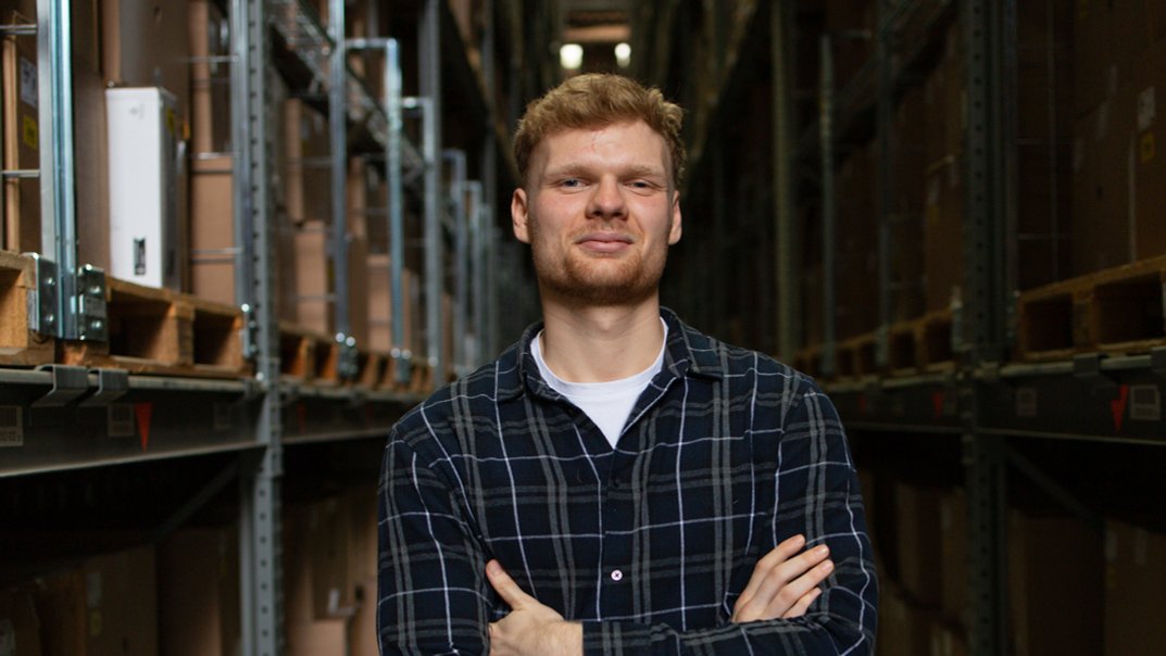 Ein junger Mann steht zwischen zwei Hochregalen 