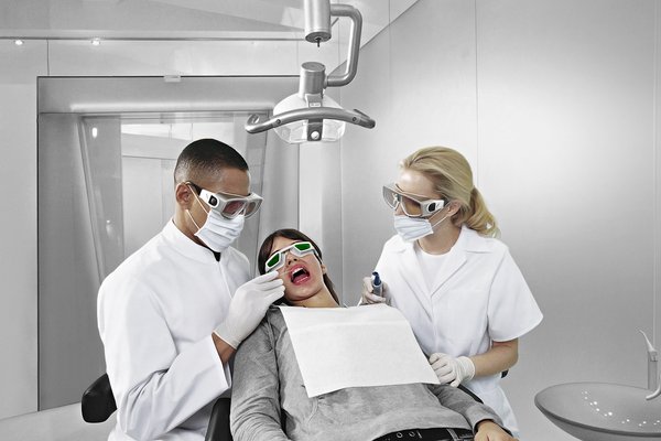 Zwei Personen führen eine Laserbehandlung durch, alle tragen Laserschutzbrillen