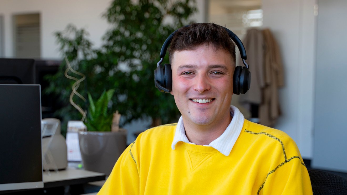 Ein junger Mann mit einem Headset lacht in die Kamera