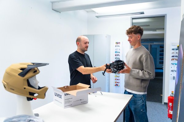 Ein uvex Werkstudent reicht einem uvex Azubi einen Radhelm