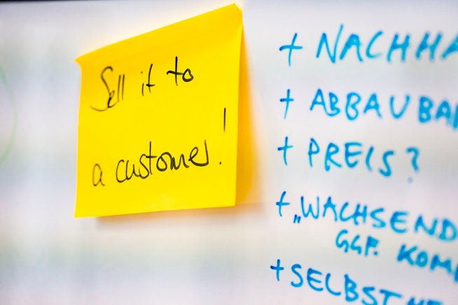 Ein Post-it mit dem Titel "Sell it" klebt an einer Tafel