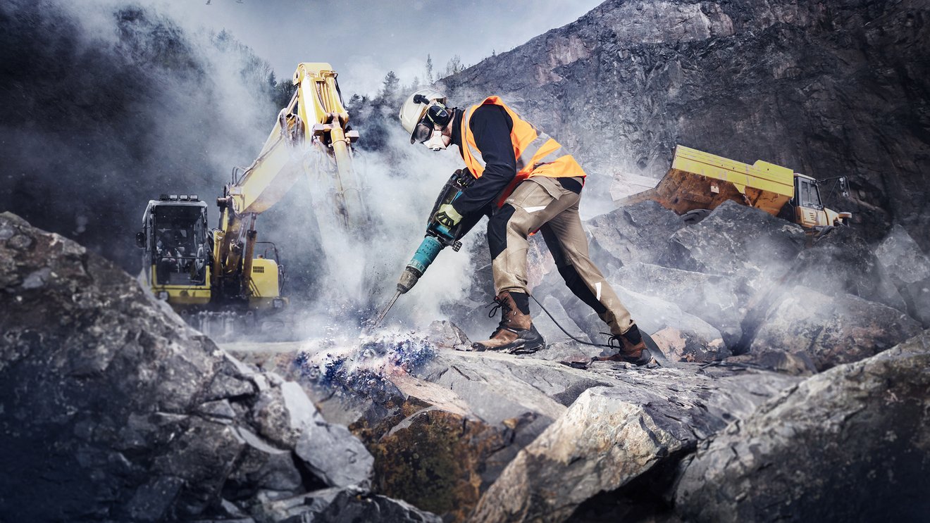 Ein Arbeiter in Warnweste arbeitet in den Bergen mit einem Presslufthammer