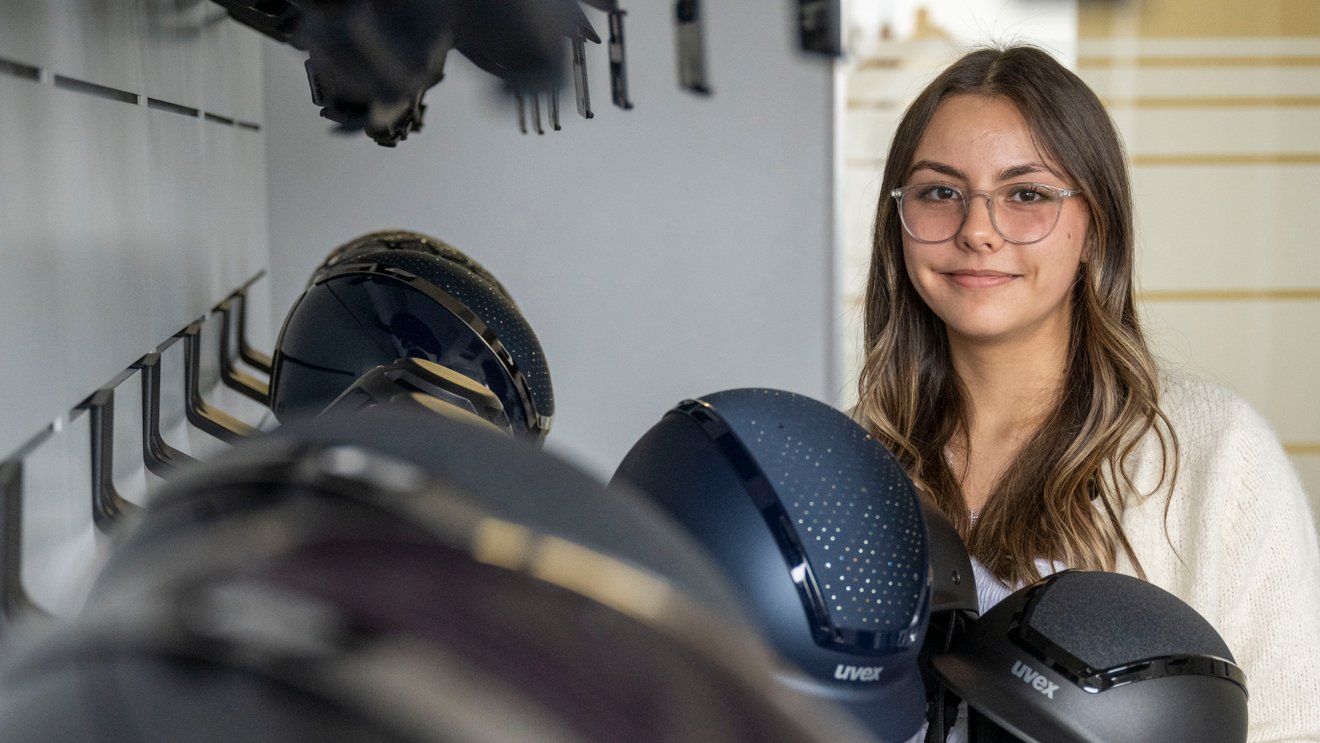 Eine junge Frau hält einen Reithelm in den Händen und lächelt