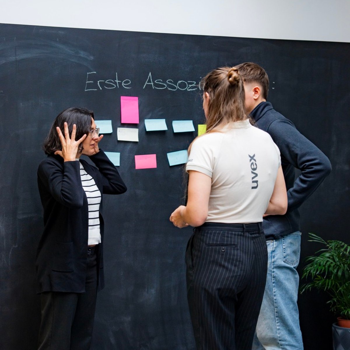 Drei Personen diskutieren vor einer Tafel, die mit Post-its beklebt ist.