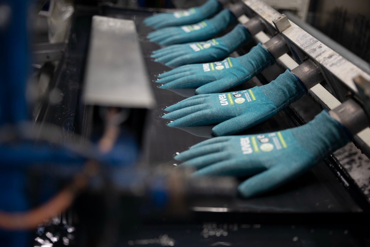 Nahaufnahme von türkisfarbenen Schutzhandschuhen von uvex auf einer automatisierten Produktionslinie während des Herstellungsprozesses.