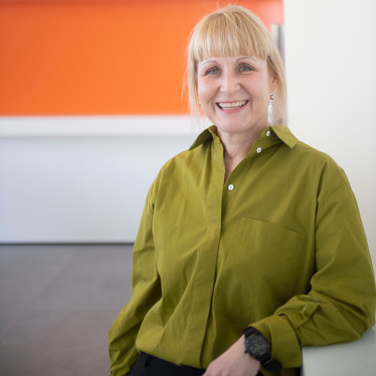 Eine Frau steht vor einem orange-grauen Hintergrund und lacht in die Kamera