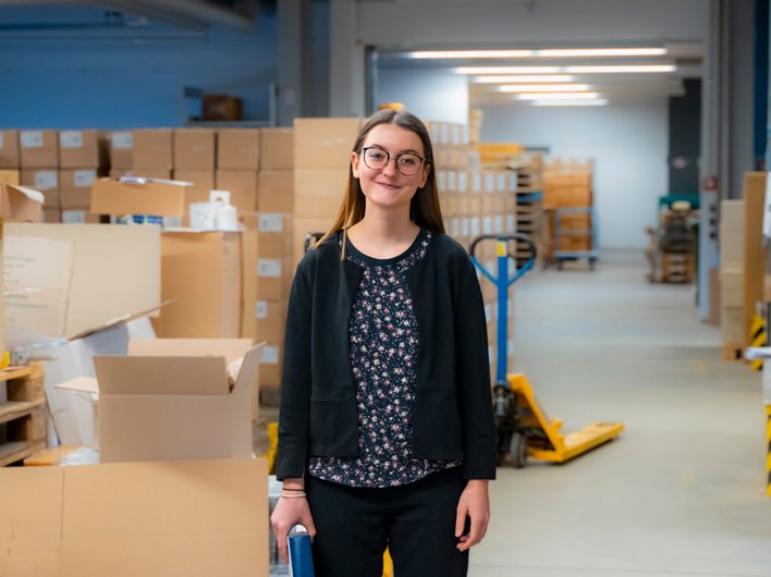 Eine junge Frau steht in einem Lager mit Kartons