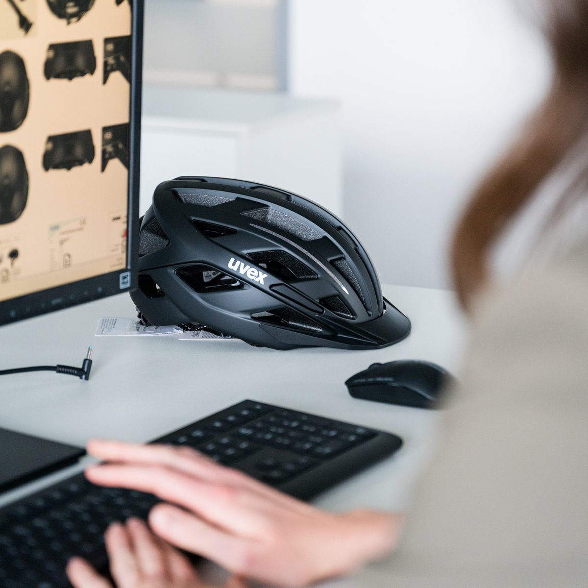 Hände die auf einer Tastatur etwas tippen. Hintergrund schwarzer uvex Radhelm