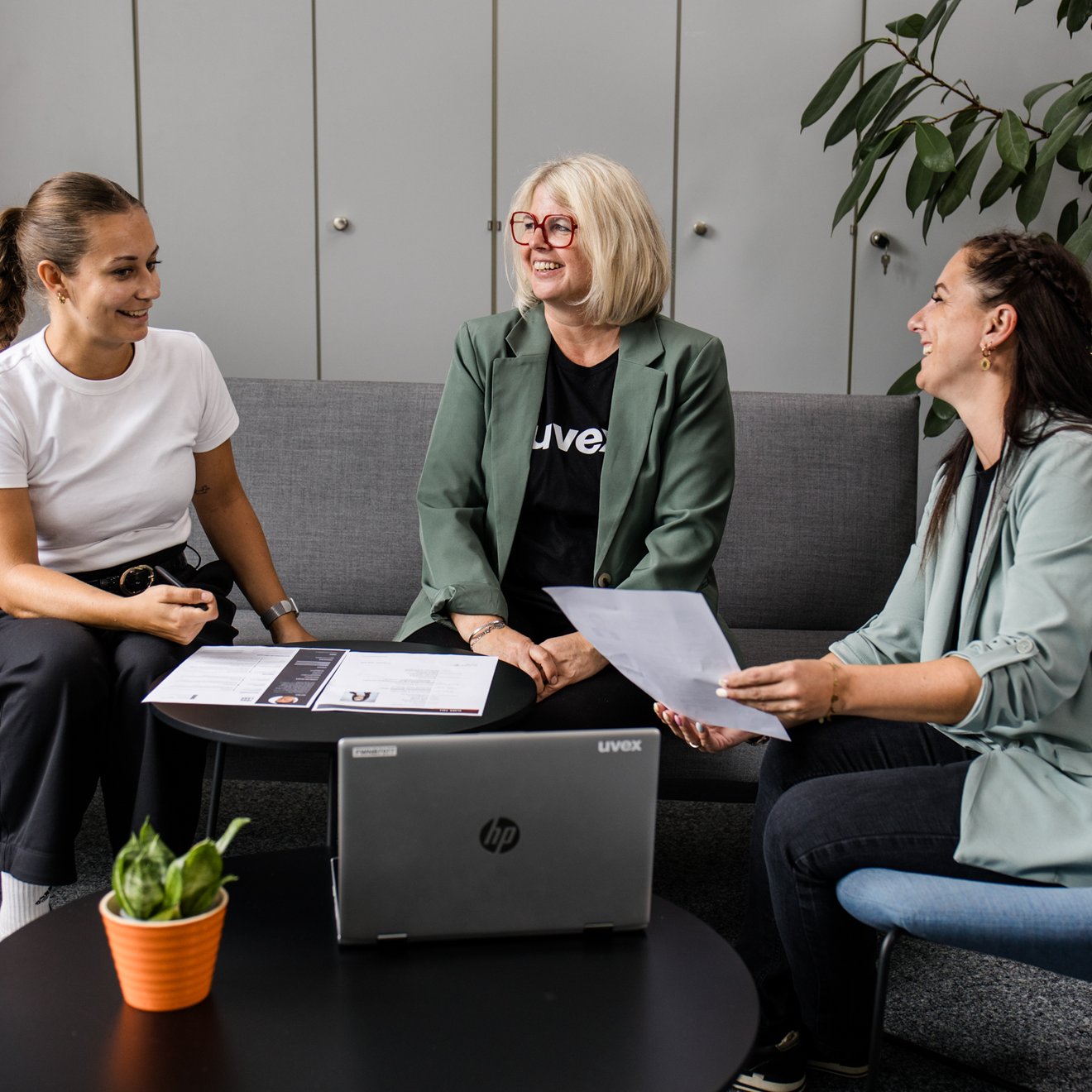 Drei Frauen sitzen an einem Tisch mit Laptop und lachen