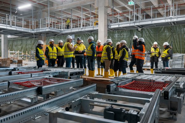 Personen in Sicherheitskleidung stehen in einem noch nicht fertigen Gebäudeteil des neuen Logistikzentrums