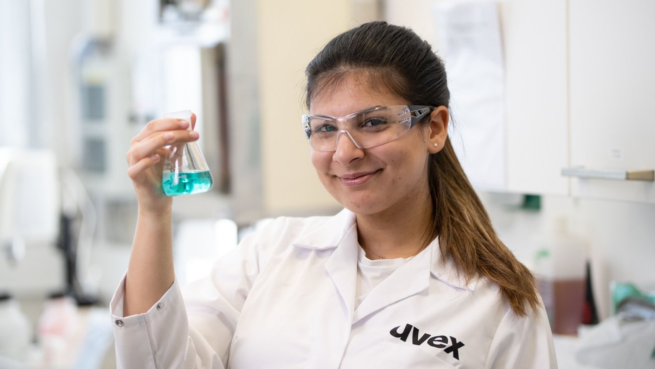 Eine Laborantin hält ein Reagenzglas in die Höhe und lächelt