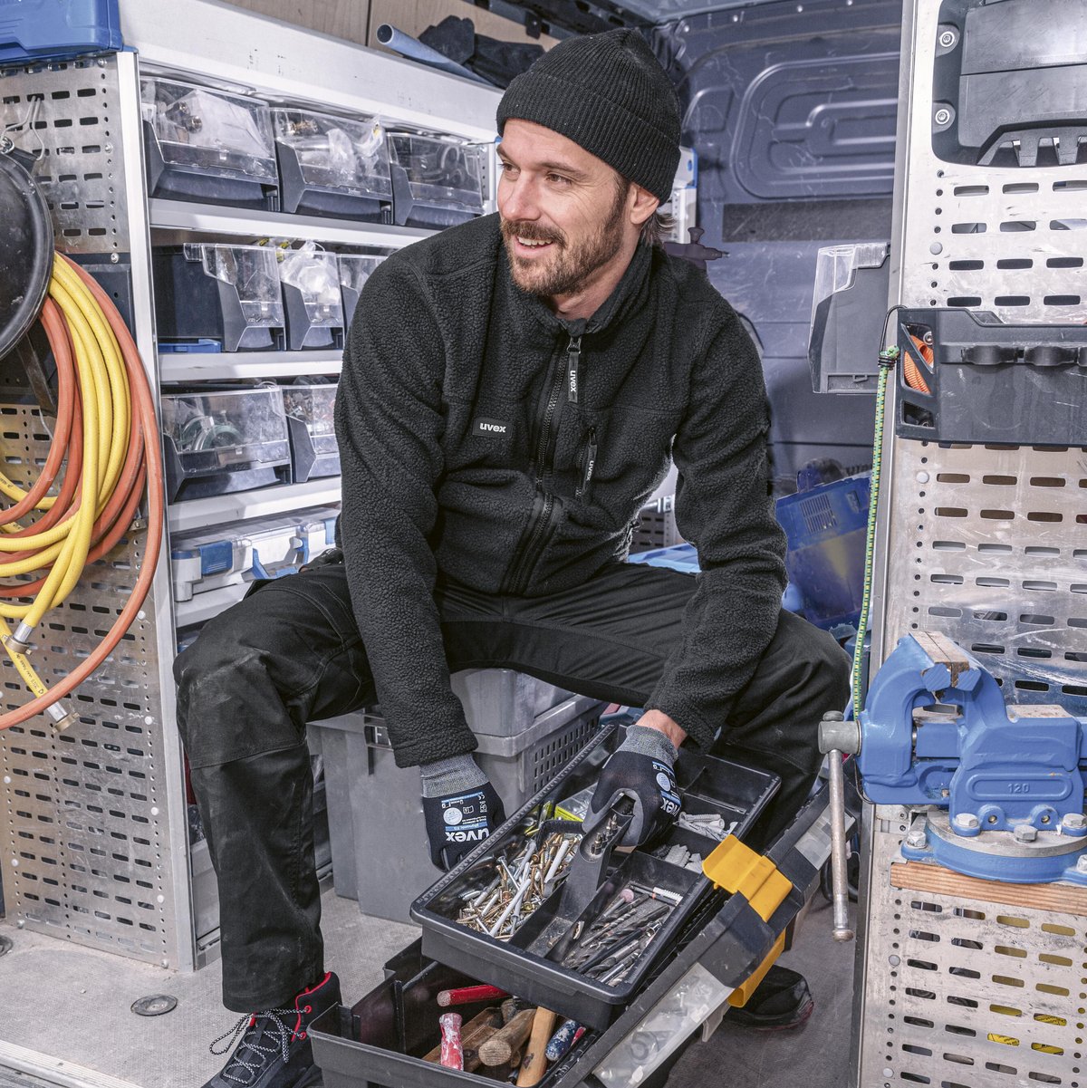 Eine Person mit Schutzhandschuhen sitzt neben einem Handwerkskasten