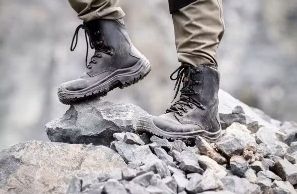 Nahaufnahme robuster Arbeitsstiefel beim Gehen über felsiges Gelände und Geröll im Außenbereich.