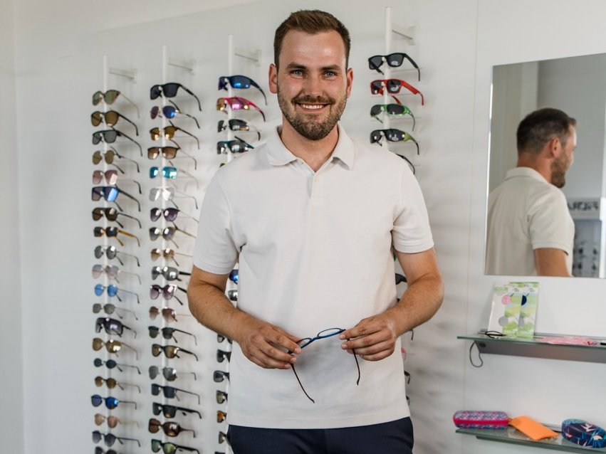 Ein uvex Trainee steht vor einem Aufsteller voller Sonnenbrillen