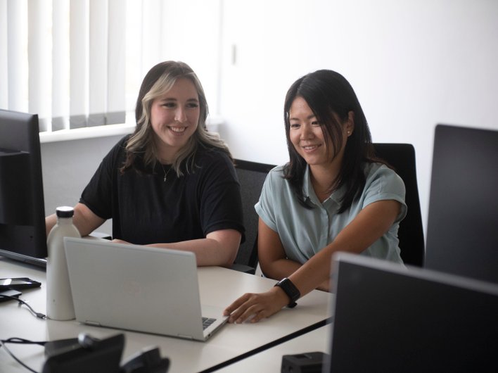 zwei Frauenarbeiten an einem Laptop und lachen