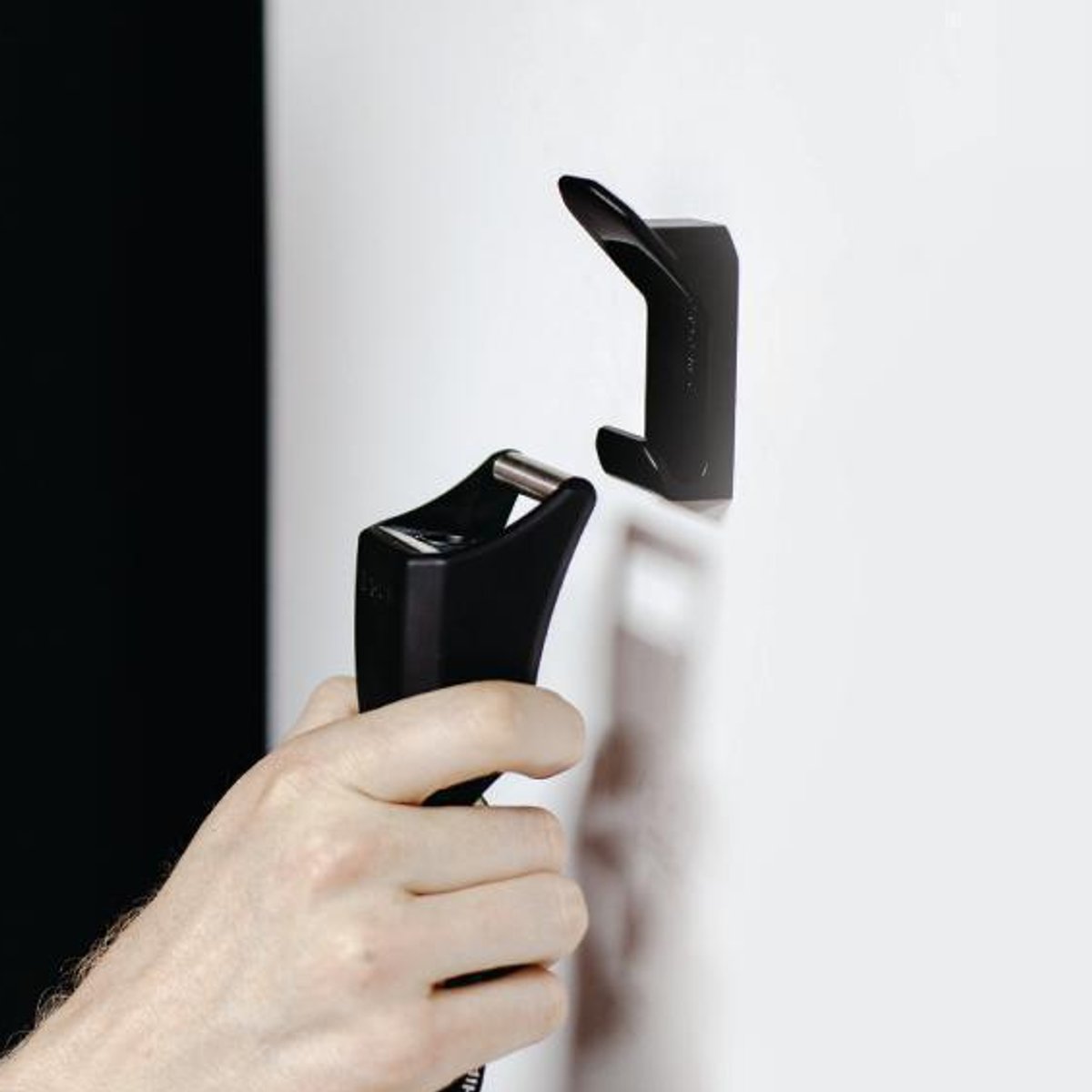 Eine Hand hängt einen schwarzen Gegenstand an der Wand auf